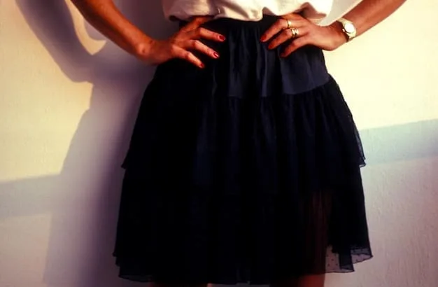 A close-up of a fashionable woman wearing a silk midi skirt, a fitted black top, and delicate gold jewelry. She is holding a clutch purse and wearing high heels, showcasing an elegant and sophisticated date night look.