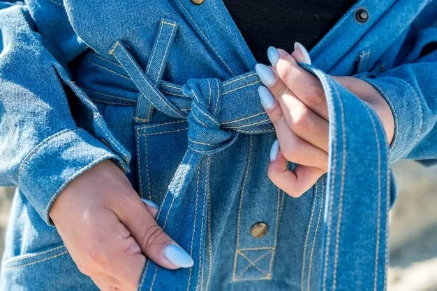 Close-up shot of a woman's hands carefully sewing a decorative patch onto a denim jacket. The patch is made from brightly colored fabric scraps, creating a visually appealing contrast. The background is blurred, with sewing supplies scattered around.