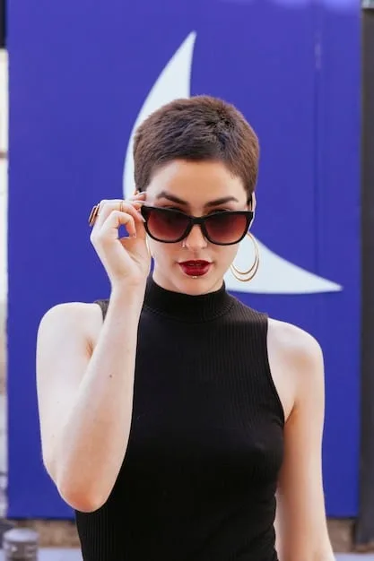 A portrait of Selena Gomez wearing oversized black sunglasses with a slightly aviator shape. She has her hair pulled back and is wearing a simple black turtleneck sweater. The background is a blurred city street.
