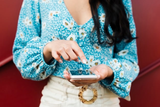 A close-up shot of a woman's hands holding a smartphone, browsing an online clothing store on the phone’s screen. The online store displays various affordable blazers and dresses similar to those worn by Meghan Markle.