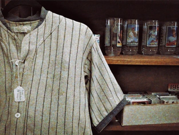 A close-up shot of a rack of vintage band t-shirts in a thrift store. The shirts feature various band logos and designs, with some showing signs of wear and tear. The lighting is warm and inviting, highlighting the unique character of each shirt.