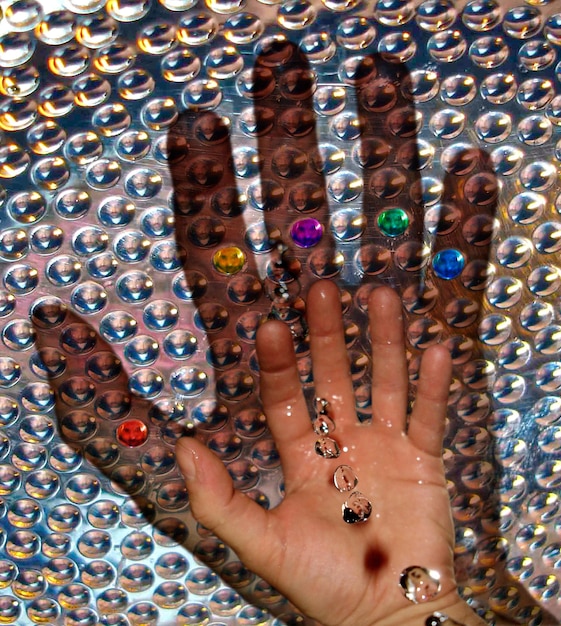 A close-up shot of a person's hands carefully gluing rhinestones onto a fabric, with various sizes and colors of rhinestones and sequins scattered around. The background is a brightly lit workspace.