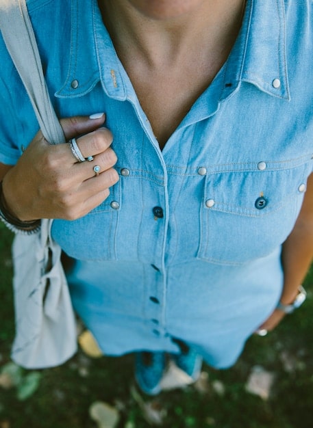 A close-up shot of a woman's outfit featuring high-waisted, light-wash denim jeans paired with a black crop top and an oversized blazer. Accessorized with a delicate gold chain necklace and chunky white sneakers.