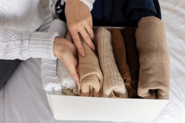 A close-up shot of a woman's hands organizing a neatly folded stack of neutral-colored sweaters and basic tops in a minimalist closet.