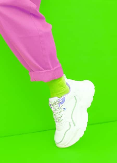 A split image featuring a pair of chunky sneakers with bold neon colors and oversized soles on one side, and minimalist white trainers with clean lines on the other, set against a gradient background.