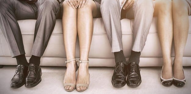 A close-up of a woman's feet showcases three different types of office-appropriate footwear: classic black leather loafers, stylish white sneakers, and elegant nude-colored block heels.