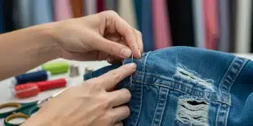 Hands repairing a denim jacket with needle and thread, symbolizing DIY fashion fixes.